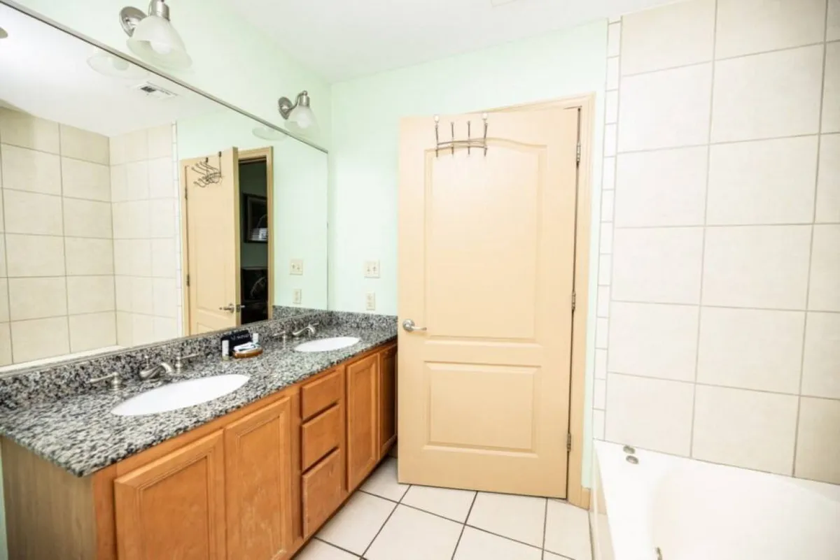 A serene bathroom with a double sink vanity, granite countertop, large mirror, and a separate bathtub, offering ample space and an organized feel.
