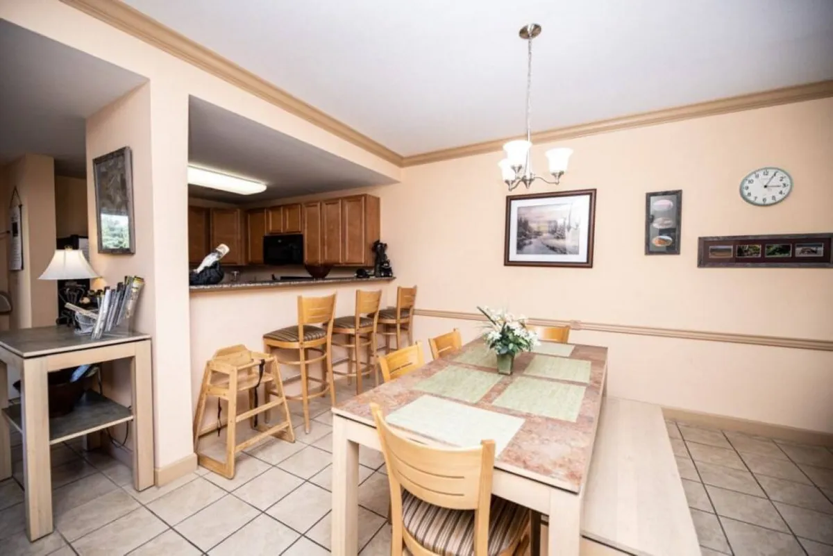 A cozy dining area features a dining table, bar stools at the kitchen counter, tasteful wall art, and a clock, highlighting the inviting ambiance for group meals and planning sessions.