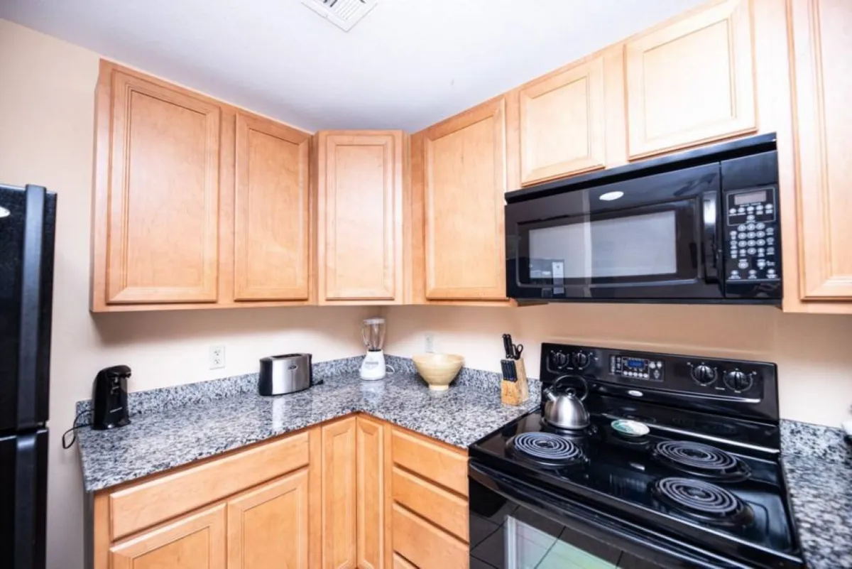 A warm and functional kitchen featuring granite countertops, black appliances, and wooden cabinets. The space is inviting and ideal for preparing at-home meals, as well as sharing time with family or friends.