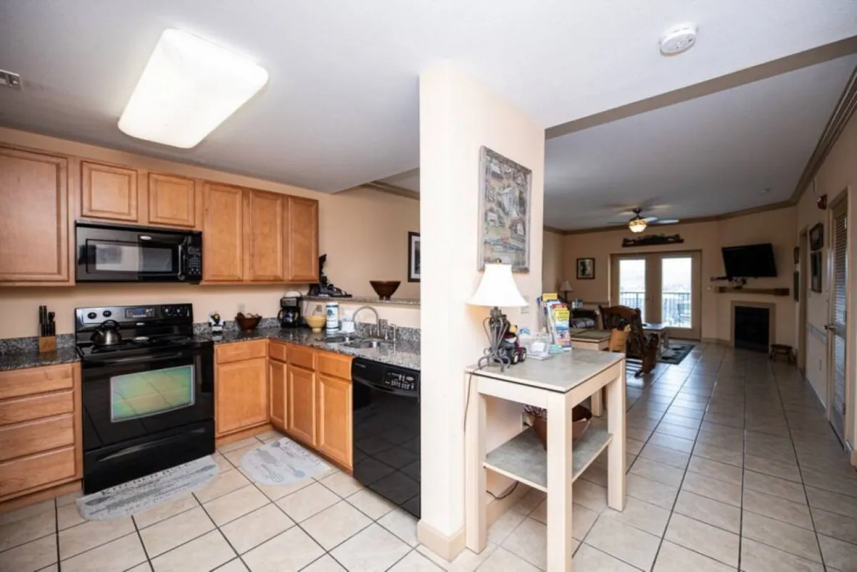 This image captures the kitchen with granite countertops, modern appliances, wood cabinetry, a visible dining area, and a glimpse of the living room entrance. The space is styled for both functionality and warmth, inviting both cooking and socializing.