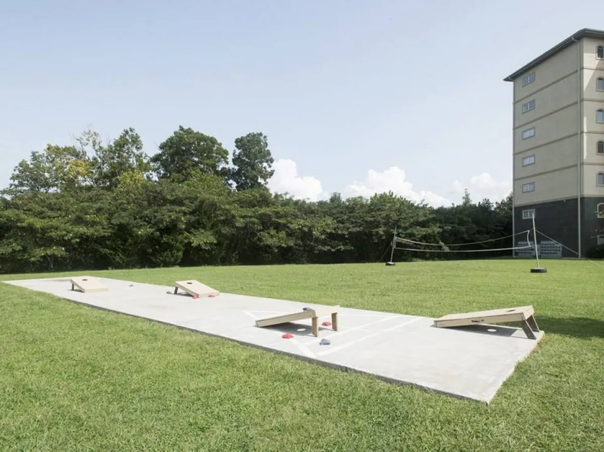 The image showcases a spacious green lawn with cornhole boards and a volleyball net, set against the backdrop of the resort’s multi-story building. Guests are engaged in friendly outdoor games, highlighting the playful and relaxed vibe of the resort grounds.
