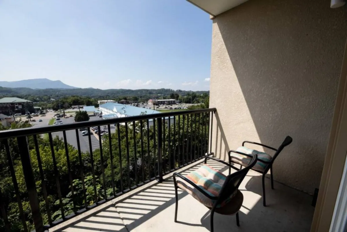 A serene balcony scene featuring a pair of chairs positioned for relaxation, overlooking a sweeping mountain vista. Lush plants add to the peaceful ambiance, and the clear view stretches to the distant Smoky Mountains, offering a tranquil place for sipping morning coffee or unwinding after outdoor adventures.