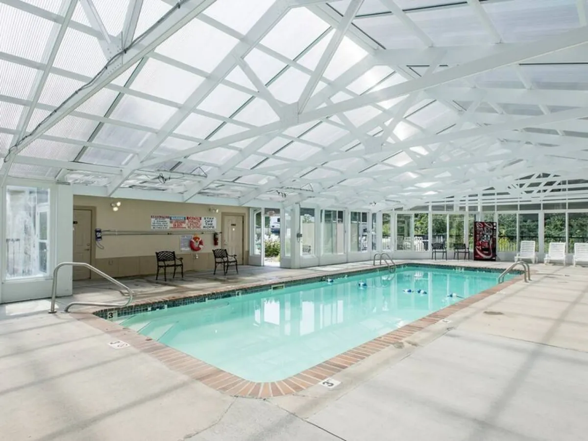 This image showcases the resort’s indoor swimming pool, featuring a transparent roof that lets natural light flood the space. There’s a seating area with chairs alongside the pool, creating an inviting, relaxed atmosphere ideal for families to swim and unwind together year-round.